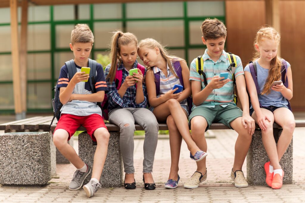 Kids sitting outside as a group looking at cell phones. Cell phone and internet safety rules for kids.