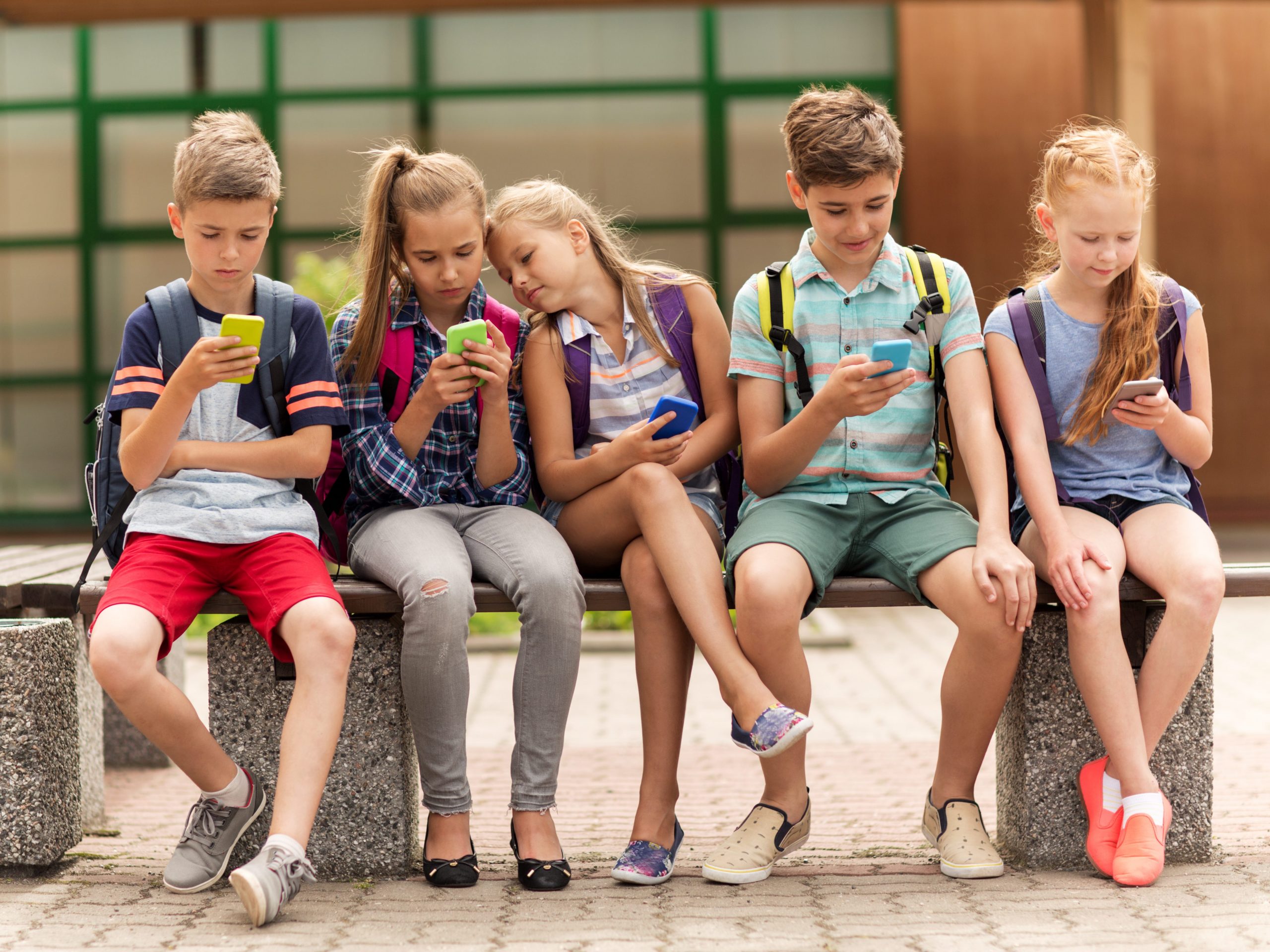 Kids sitting outside as a group looking at cell phones. Cell phone and internet safety rules for kids.