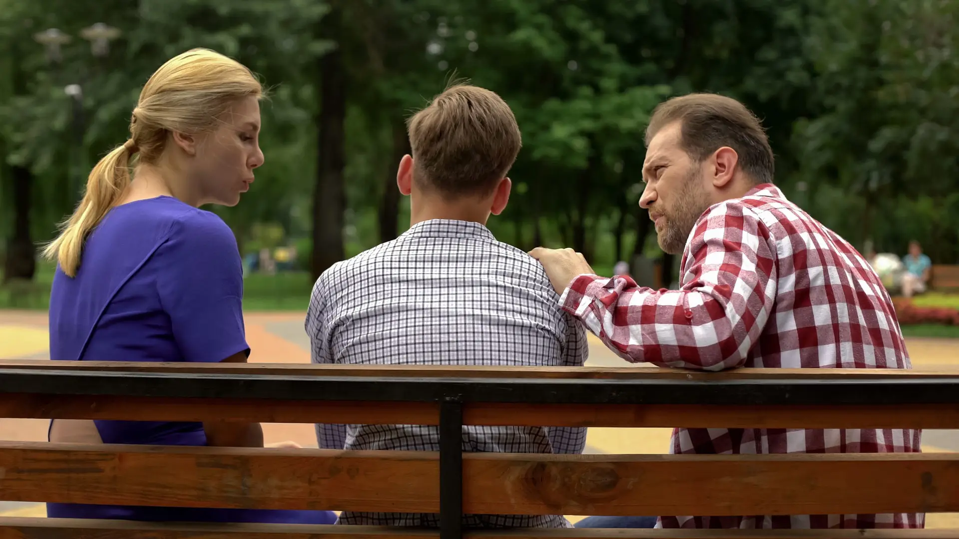 Parents talking with son on bench in park, supporting teen in time of trouble