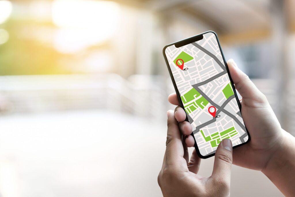 A person holding a smartphone showcases how GPS works, displaying a digital map with location pins. The softly blurred background hints at an indoor space basking in natural light, underscoring how this technology keeps your kids safe and secure.