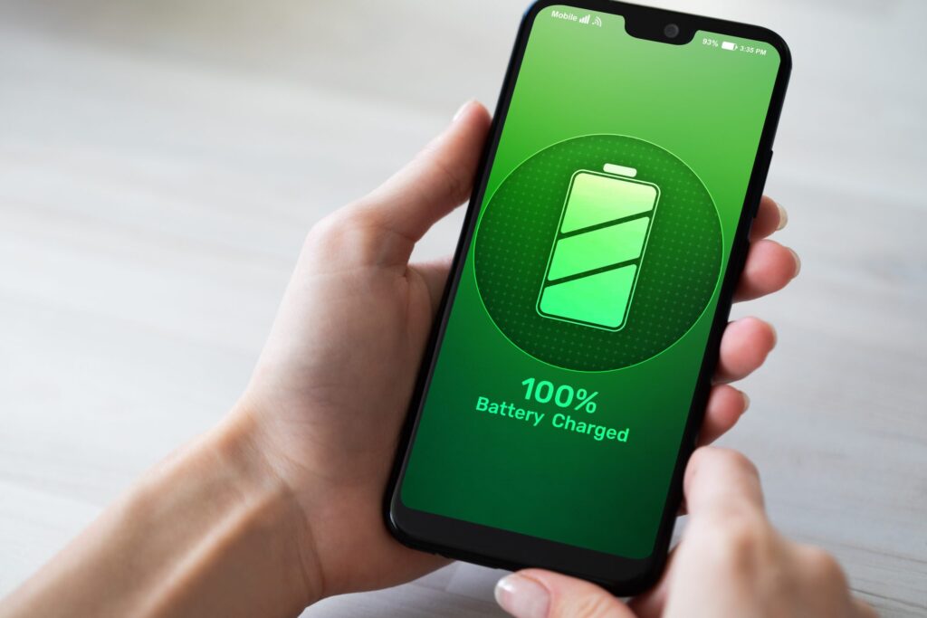 A person holding a smartphone showing off its fully charged battery at 100% on a green screen, exemplifying success in how to improve your phone's battery life.