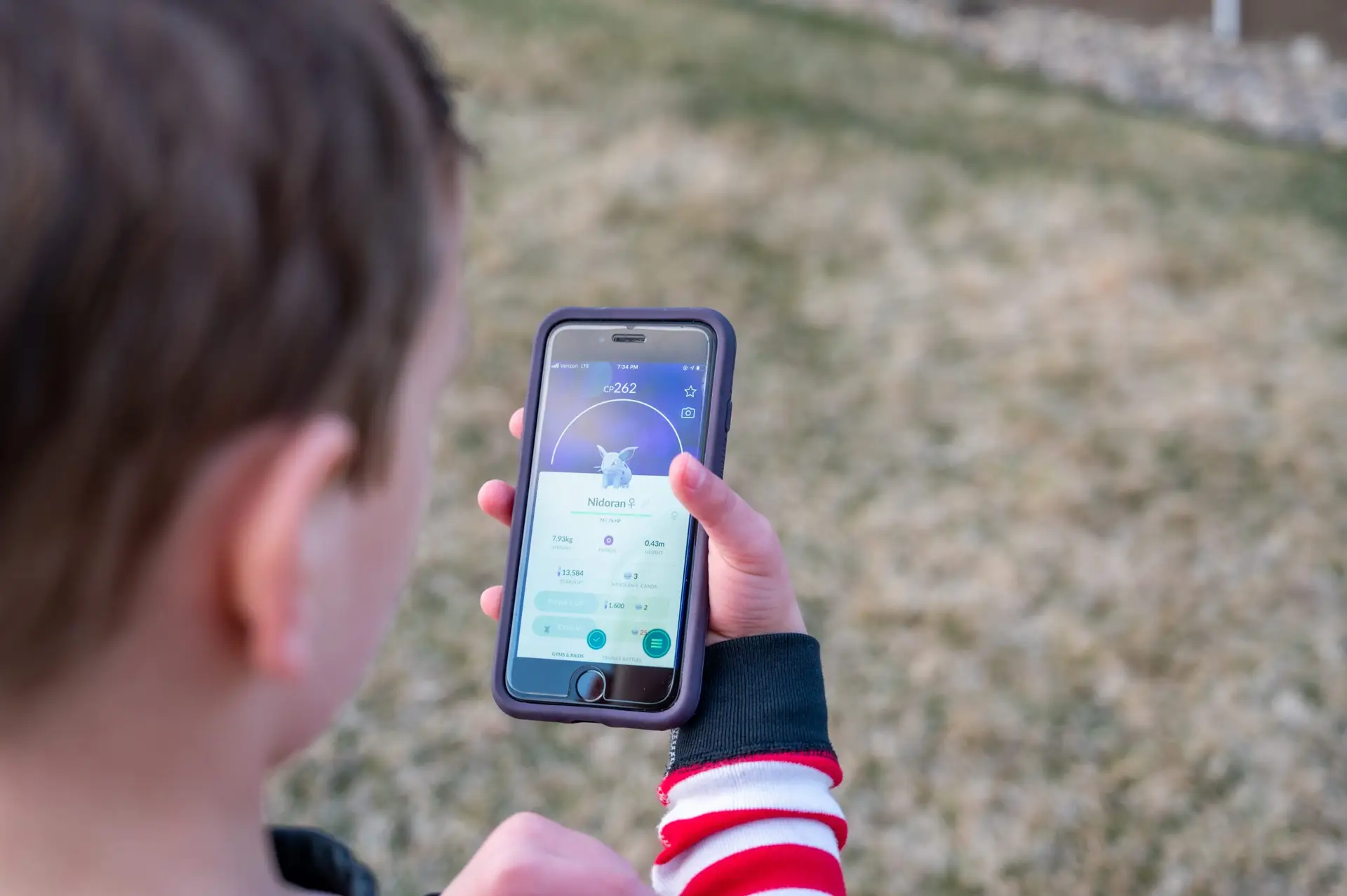 A person holds a smartphone displaying a Pokémon game with Nidoran ♀ on the screen, set against a grassy outdoor backdrop. Exploring if Pokémon is safe for kids and your privacy might add to the adventure.