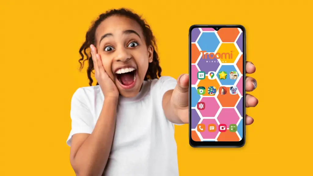 A smiling child holds a smartphone towards the camera, showing a colorful honeycomb-patterned screen with app icons. With an excited expression and wearing a white shirt, they seem ready to show you how easy it is to change your wallpaper. The background is solid yellow.