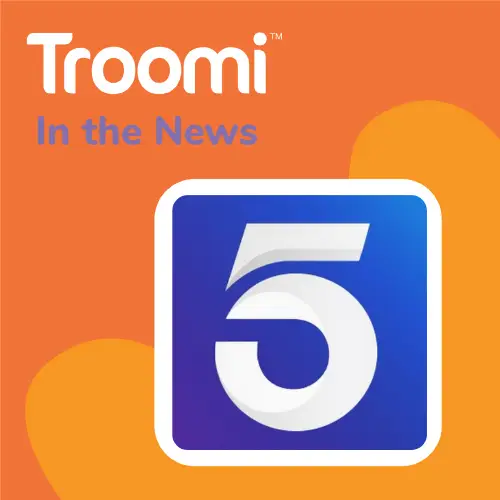 Orange background with the word Troomi and In the News at the top. Below is a blue and purple square with the number 5 in white. An orange heart shape is partially visible behind the square, echoing Troomi’s safety features highlighted in Digital Trends.