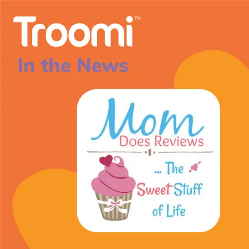 The image showcases the Troomi logo with "In the News" above it, alongside Mom Does Reviews' logo featuring a cupcake illustration and their tagline, "...The Sweet Stuff of Life." All set against an orange background adorned with abstract shapes.