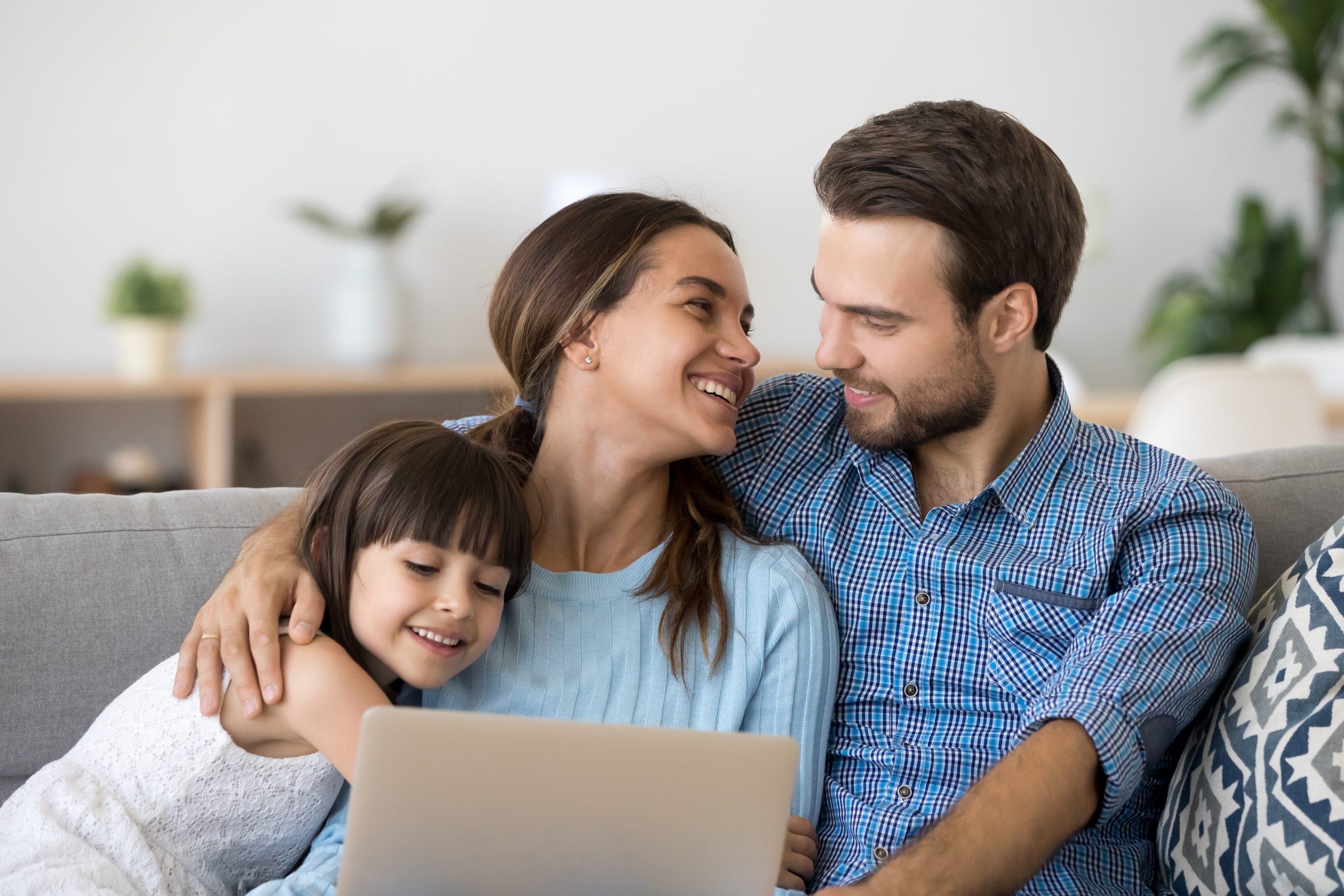 A happy family of three sits on a couch, smiling as they explore "Your Guide On How to Find Anything on the Internet" together. The woman is in the center, with a young girl snuggled on her left and a man embracing her from the right. The room is cozy with soft lighting and decorations in the background.