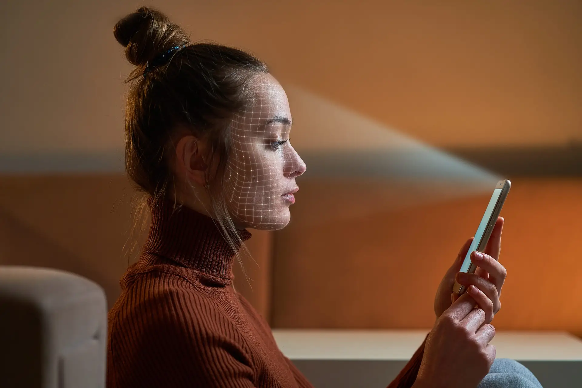 A woman in a brown turtleneck demonstrates how facial recognition works on her smartphone. A digital grid pattern is projected on her face, highlighting the scanning process. She sits indoors, against a neutral background, illustrating the seamless integration of technology into daily life.