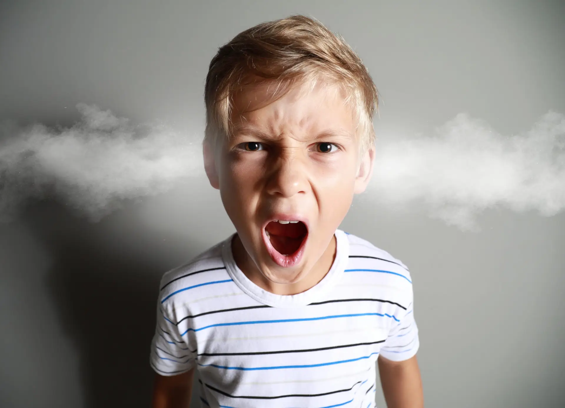 A young boy with blond hair and a striped shirt appears to be displaying anger issues, with steam graphics coming out of his ears against a gray background. His open mouth emphasizes his intense expression.