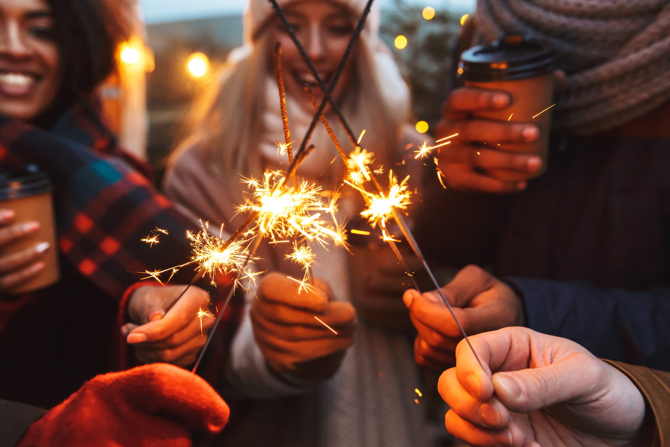 A group of people holding sparklers creates a festive atmosphere, embodying the spirit of keeping New Year’s resolutions. Bundled in warm winter clothing, they savor hot drinks, while the softly blurred background suggests an outdoor celebration welcoming new beginnings.