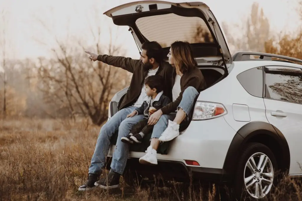 A family of three enjoys their SUV's open trunk, parked in a grassy field. The father points into the distance, capturing the essence of autumn with vibrant foliage around. It's a perfect moment to reflect on freedom and possibly learn something new, like escaping entrapment from within.