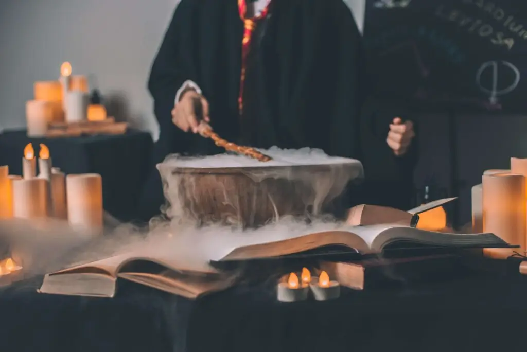 A person in a wizard-like robe stirs a steaming cauldron with a wand, surrounded by books, candles, and magical decor. The scene is mystical and dimly lit, perfect for sparking imagination or introducing Harry Potter activities for kids.