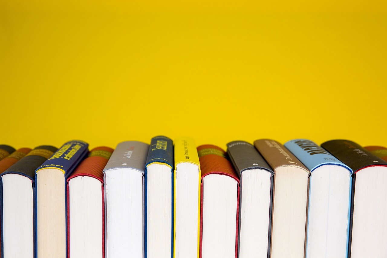 A row of sports books for kids stands vertically against a bright yellow background. Only the top halves are visible, revealing a lively mix of colors and textures on the spines, inviting young readers into adventures and tales from the world of athletics.