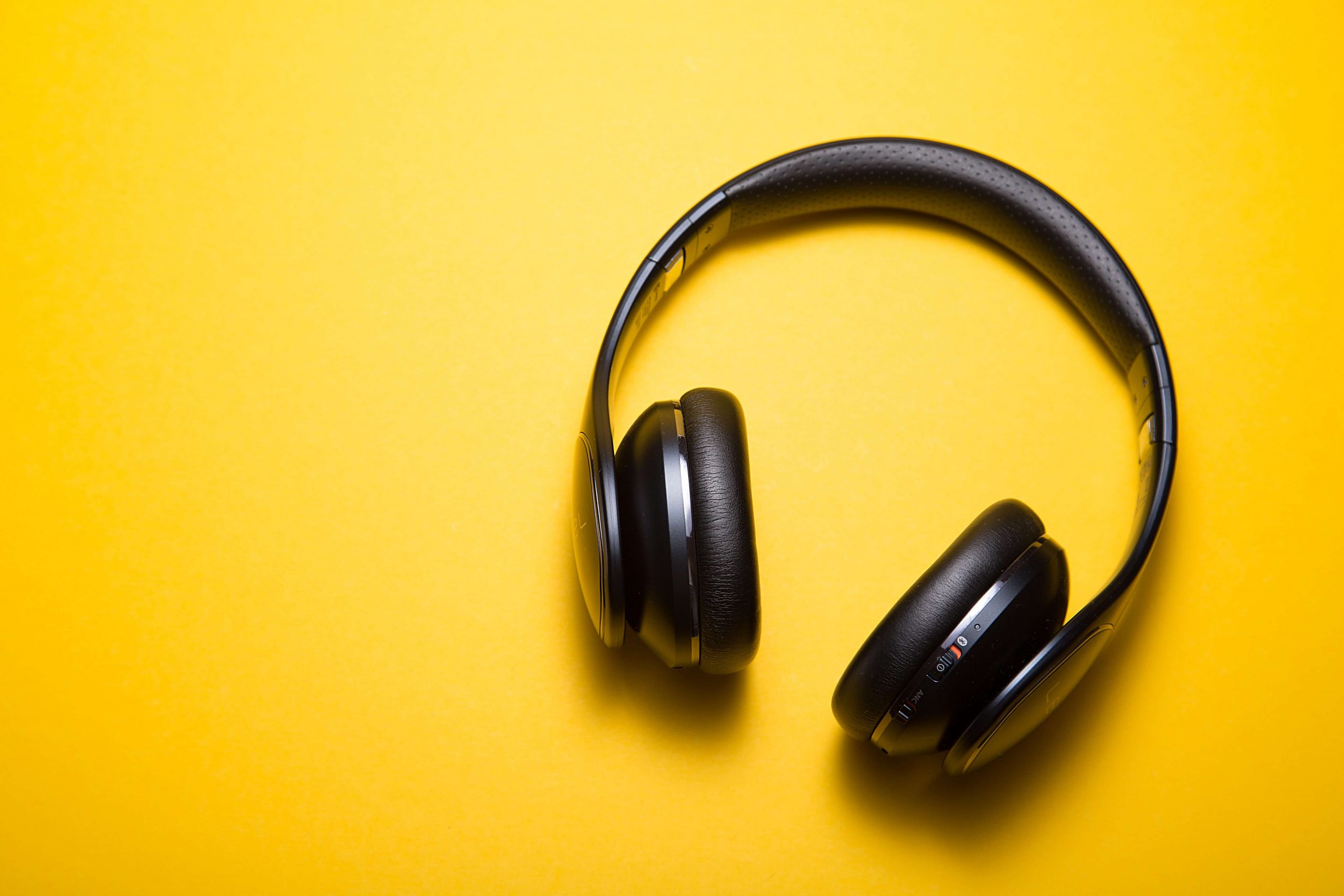 A pair of black over-ear headphones resting on a bright yellow background, perfect for enjoying summer songs for kids. The headphones are slightly tilted with the ear cups facing up.