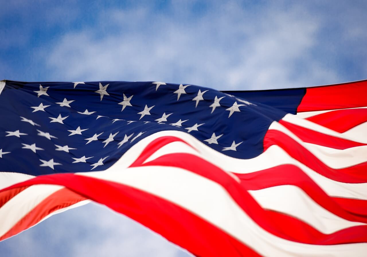 The image captures an American flag waving gently in the breeze against a clear blue sky, reminiscent of 4th of July crafts for kids, where vibrant red, white, and blue colors bring the stars and stripes to life.