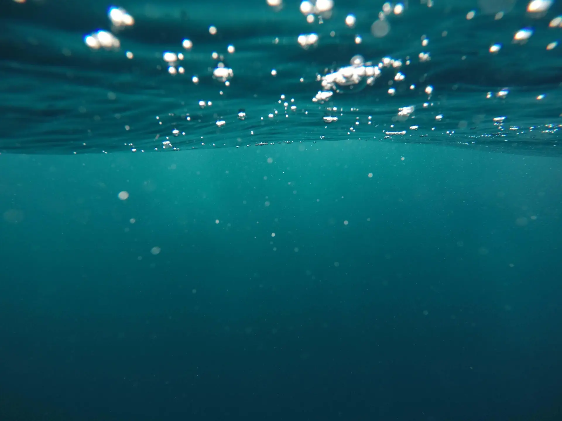 Underwater view with a turquoise hue, showing numerous air bubbles suspended in the water. The scene evokes a sense of calm and immersion, reminiscent of ocean adventures in summer movies for kids.