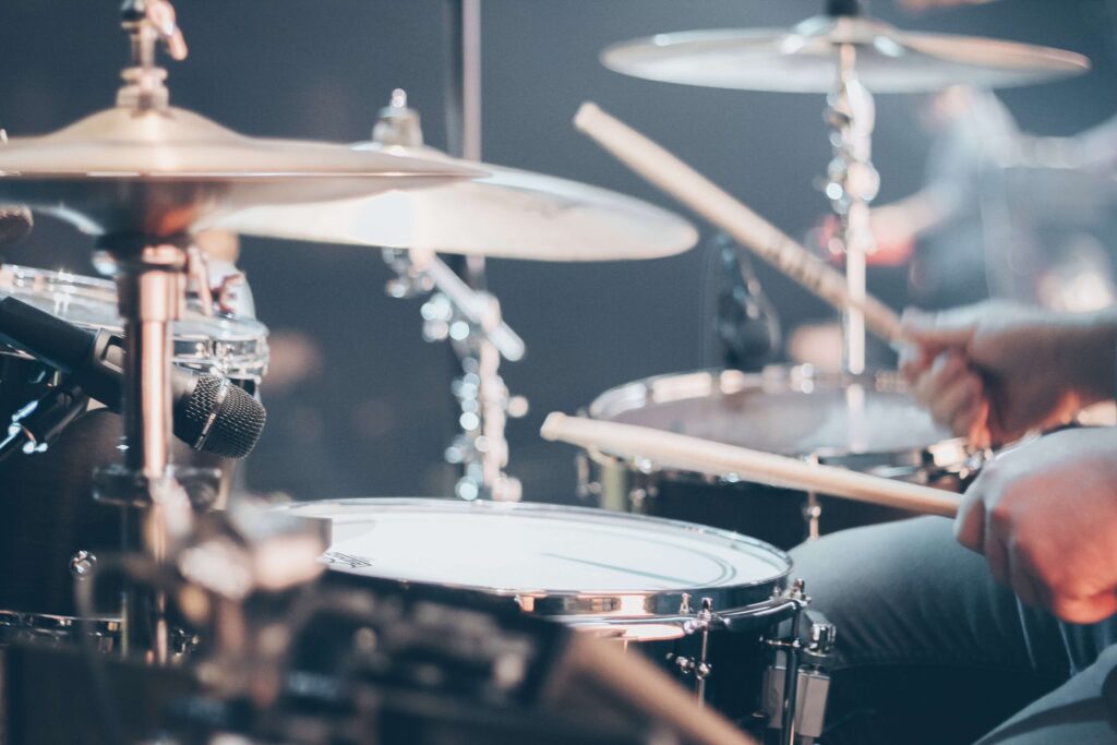 A close-up of a drummer's hands playing on a drum set for kids, with cymbals gleaming. The focus is on the lively movement of the drumsticks, capturing a dynamic action shot. The background blurs, highlighting the vibrant musical performance ambiance perfect for young musicians.