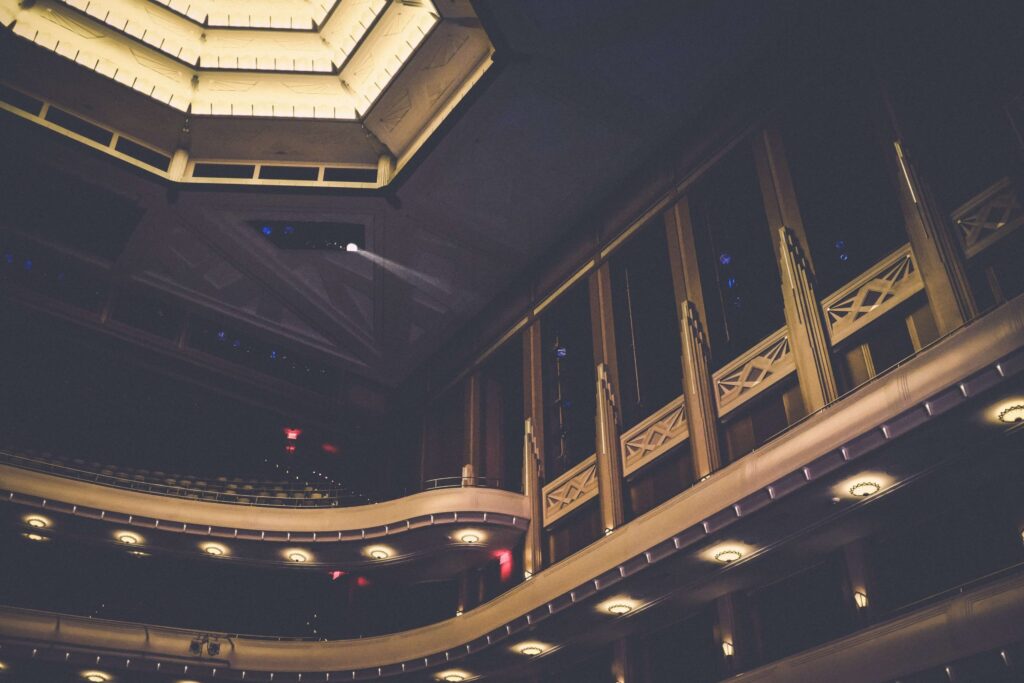 The interior of the theater exudes charm with its multiple balconies adorned in ornate railings, soft lighting, and a hexagonal ceiling feature. This dimly lit venue is ideal for immersing viewers in kid-friendly musicals, highlighting every architectural detail.