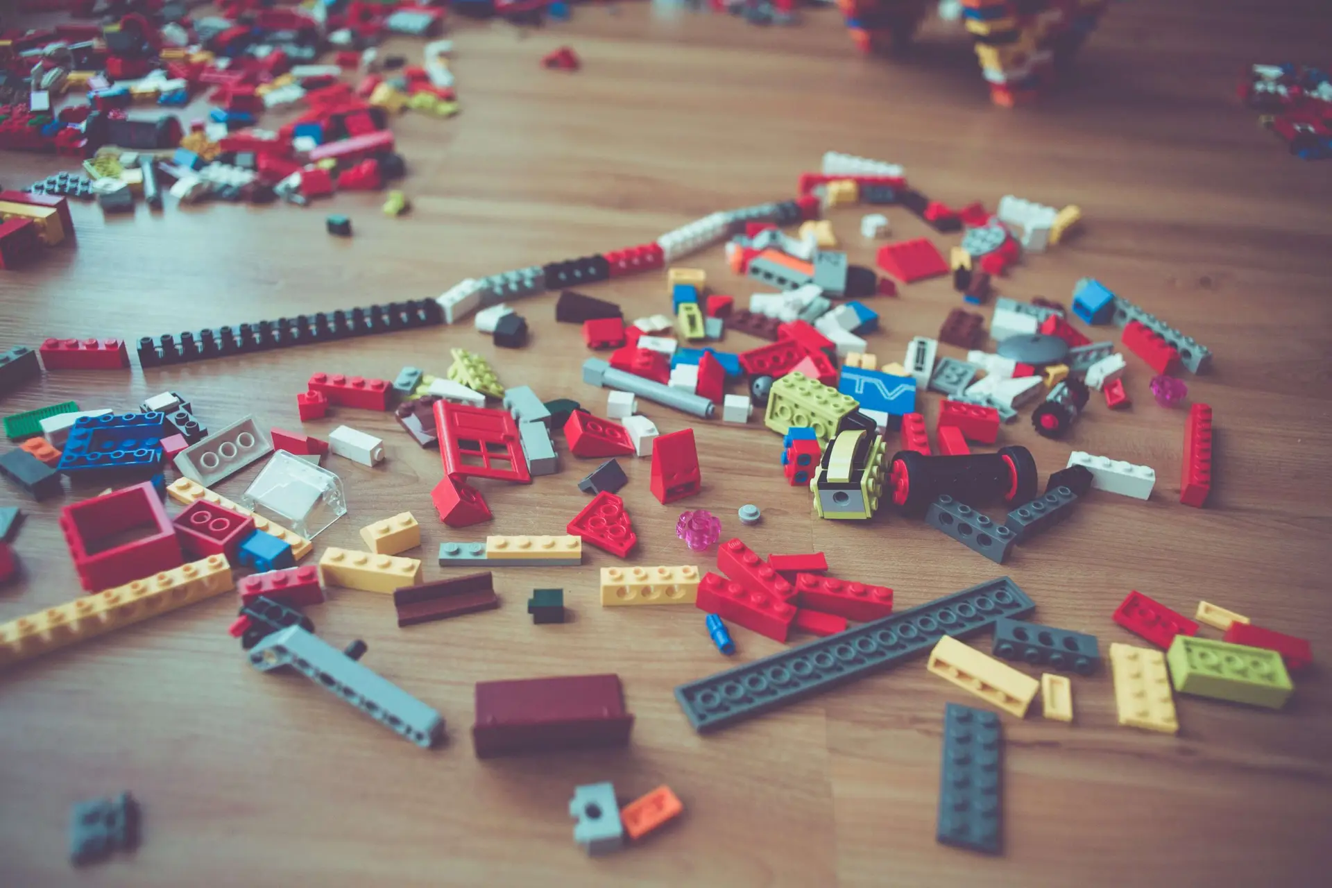 A scattered collection of colorful LEGO pieces on a wooden floor, reminiscent of memory games for kids, includes blocks in red, blue, yellow, and gray.