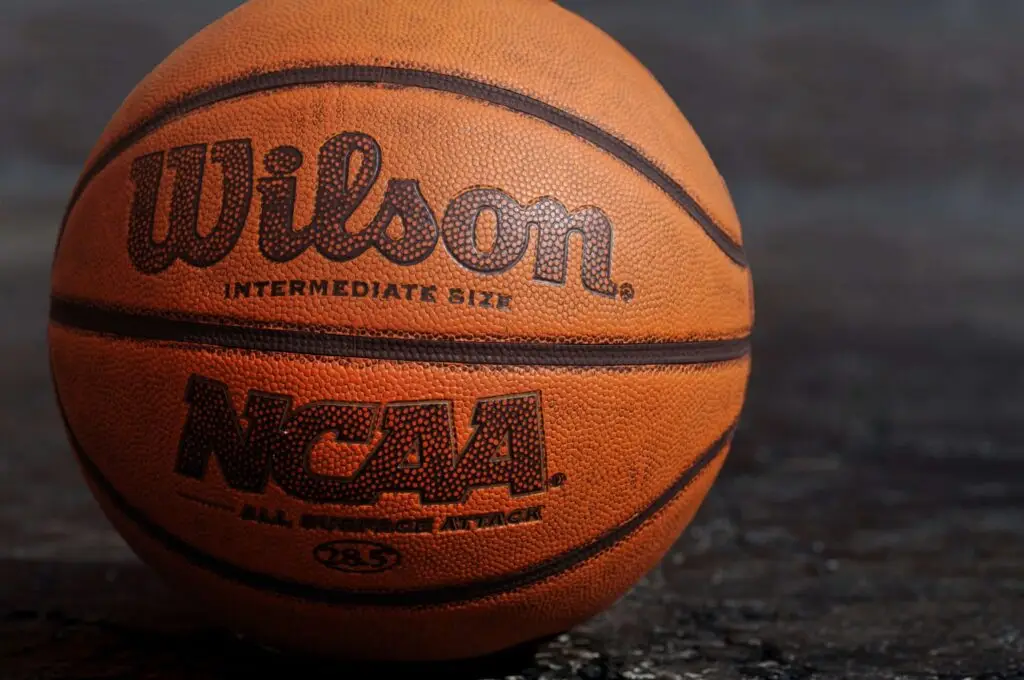 Close-up of a Wilson basketball featuring the NCAA logo and INTERMEDIATE SIZE text, perfect for basketball games for kids. The ball rests on a textured dark surface, highlighting its vibrant orange and brown patterns.