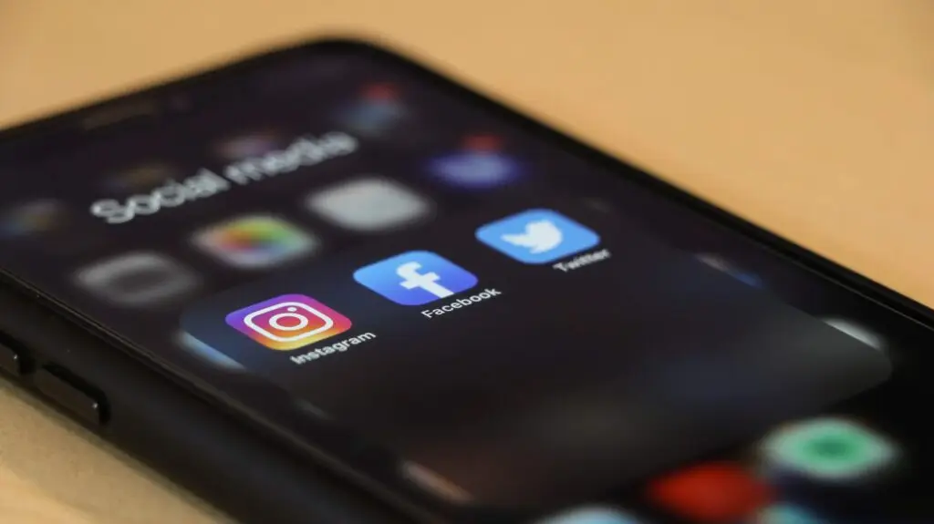 A smartphone screen showcases a folder labeled Social Media with icons for Instagram, Facebook, and Twitter. This digital realm is where the ever-evolving story of how social media affects kids unfolds, as the phone rests on a light-colored surface.