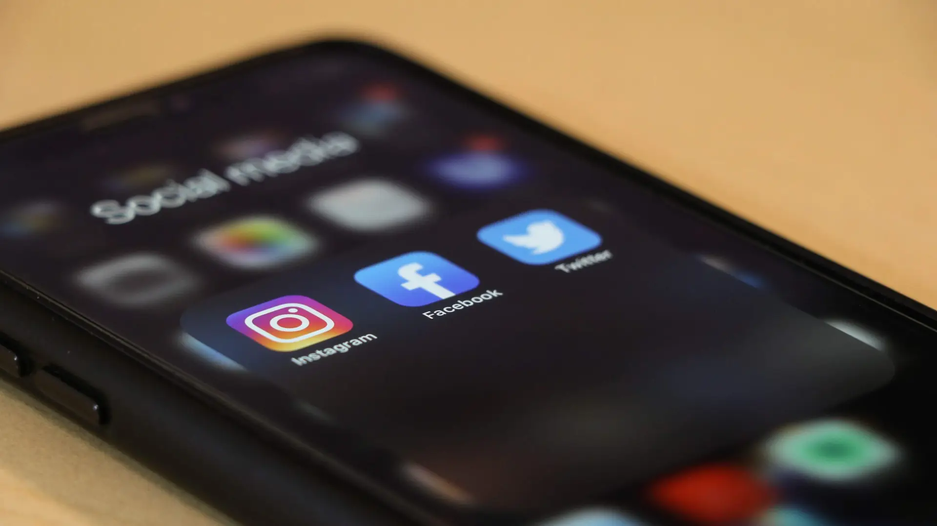 A smartphone screen showcases a folder labeled Social Media with icons for Instagram, Facebook, and Twitter. This digital realm is where the ever-evolving story of how social media affects kids unfolds, as the phone rests on a light-colored surface.