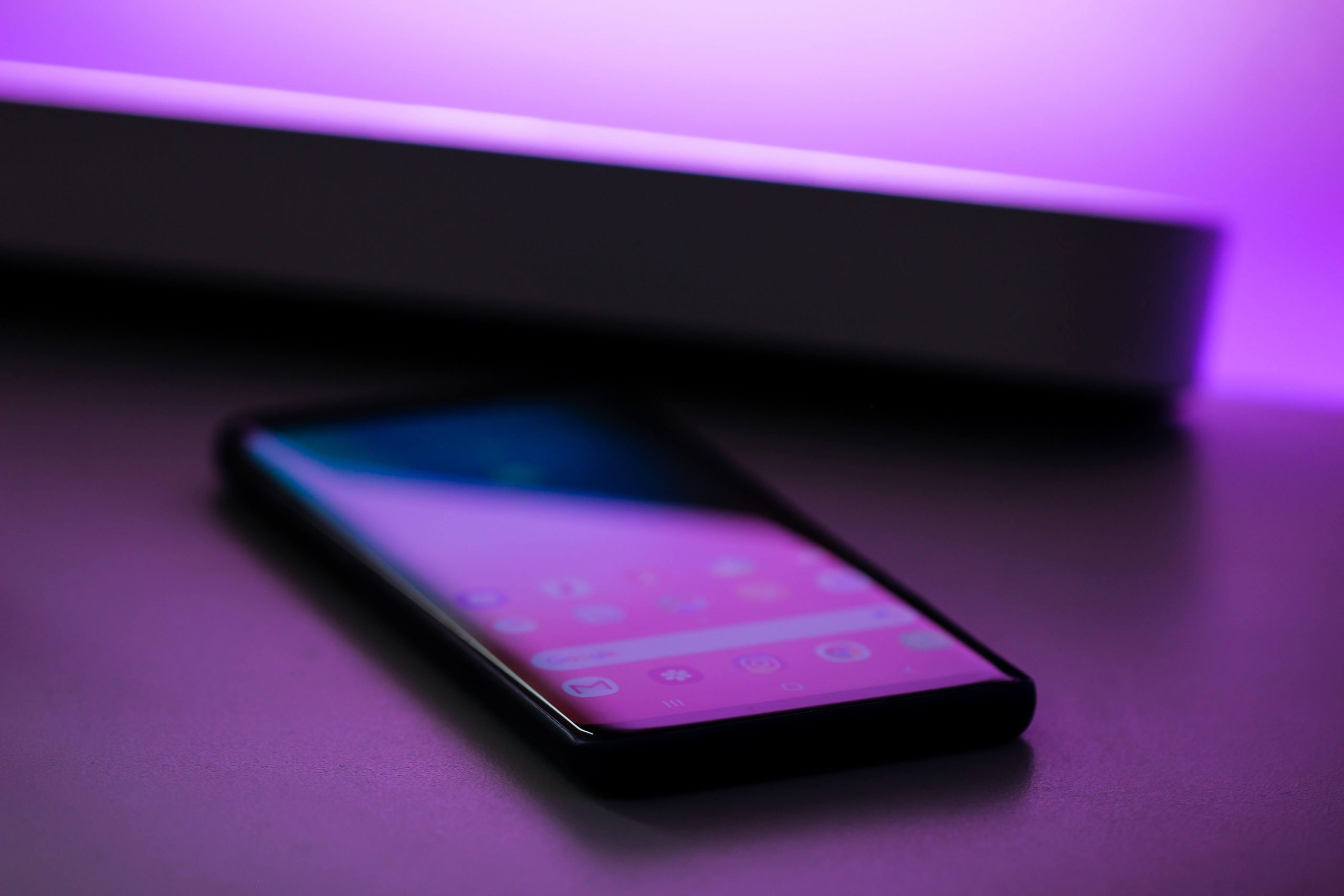 A safe smartphone for kids with a glowing screen lies on a surface, lit by a purple light in the background.