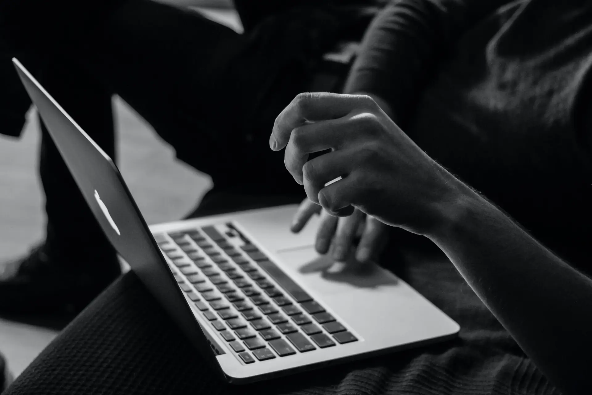 In a black-and-white image, a person types with one hand while gesturing expressively with the other. The highlighted keyboard suggests they might be pondering complex issues, such as whether cyberbullying is protected by freedom of speech.