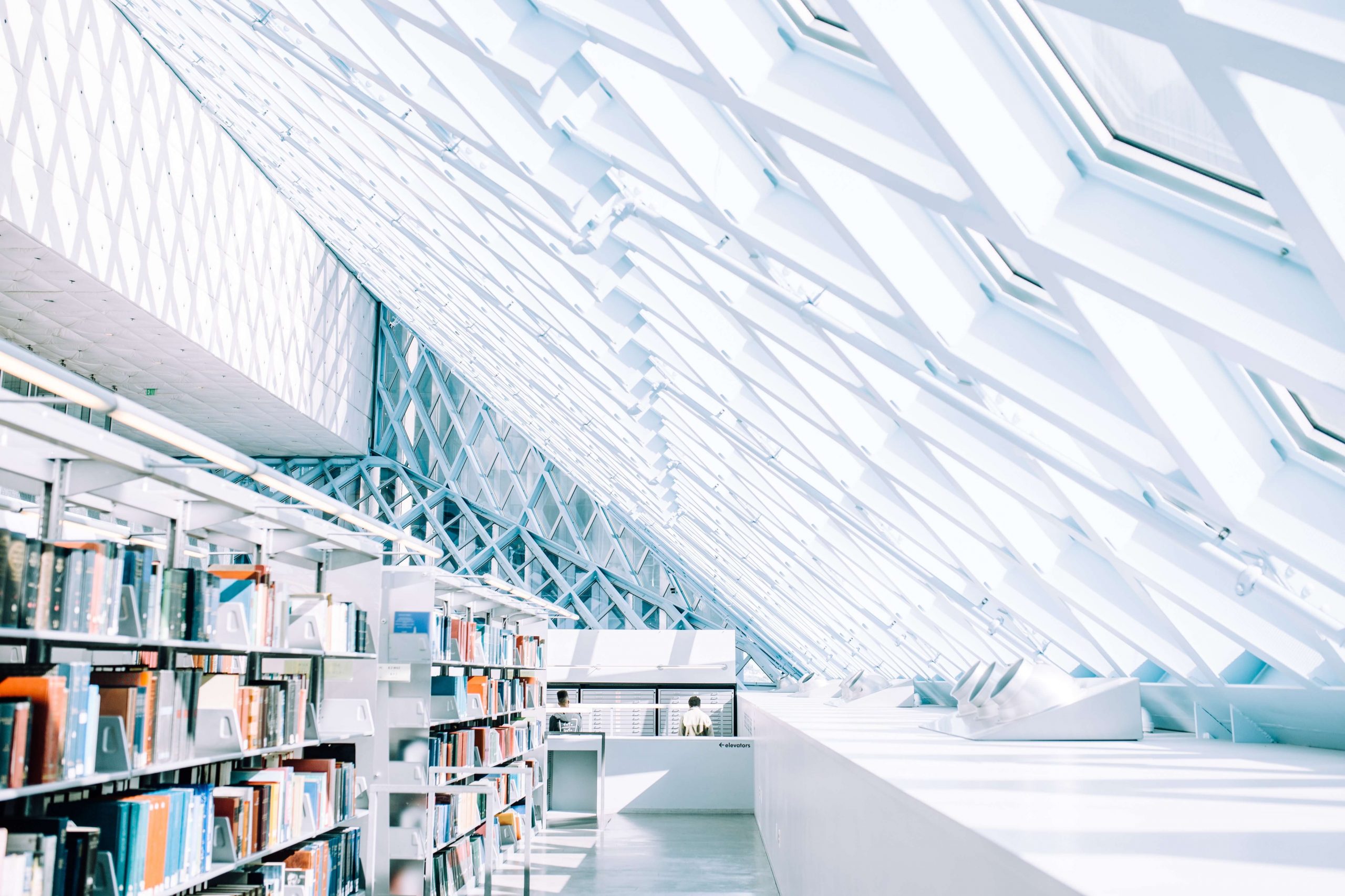 A modern library interior with large, slanted glass windows creates a bright and airy atmosphere. Bookshelves filled with colorful, award-winning children's books line one side, while natural light floods the space.