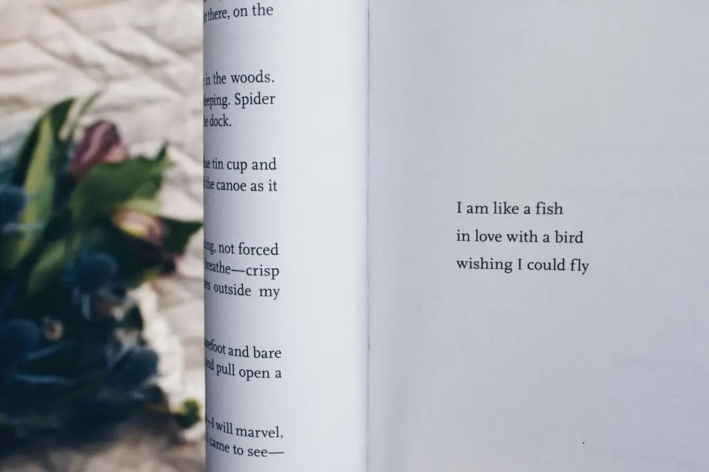 A close-up of an open book, perfect for teens exploring poetry, features poetic text on the right page reading, "I am like a fish in love with a bird wishing I could fly." Blurred leaves and flowers add depth to the background on the left.