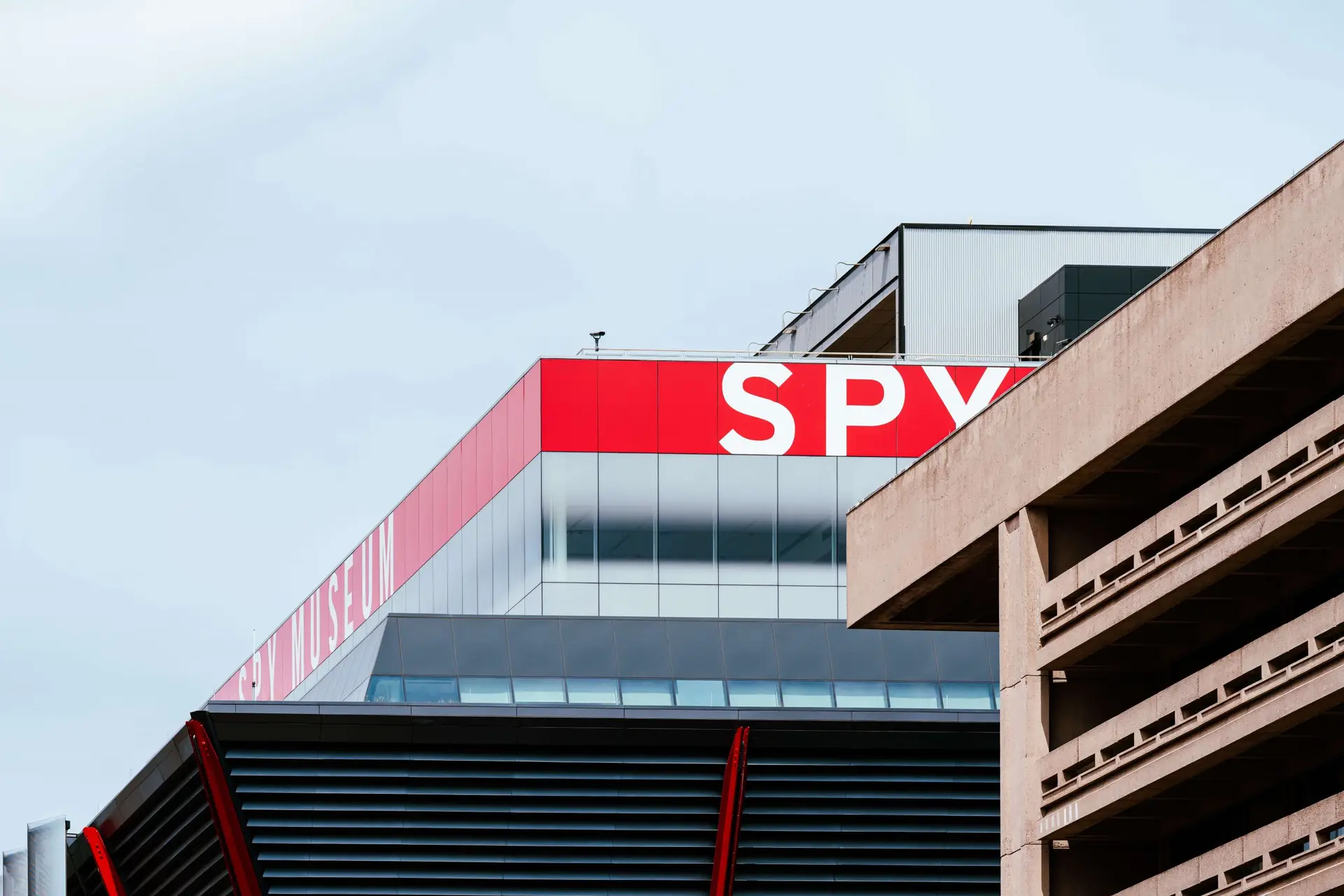 A modern building with large red and white signage that reads SPY stands prominently, resembling a hub for spy books for teens. The design, featuring glass panels and industrial elements, complements the mysterious allure under the overcast sky.