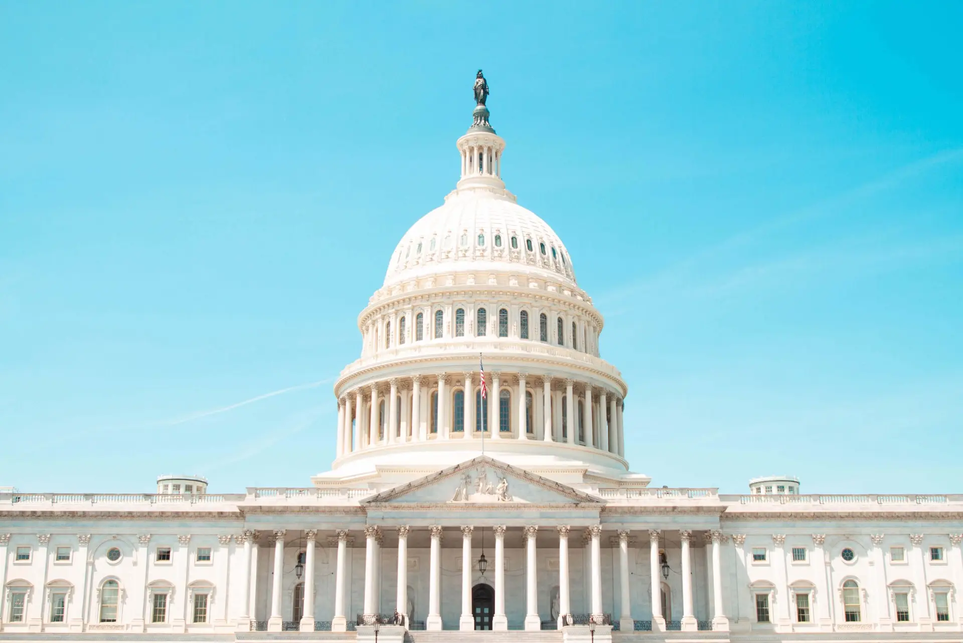 The image shows the United States Capitol building in Washington, D.C., featuring its prominent white dome, columns, and classical architectural details against a clear blue sky—a symbol of where crucial social media legislation and other pivotal laws are debated and enacted.