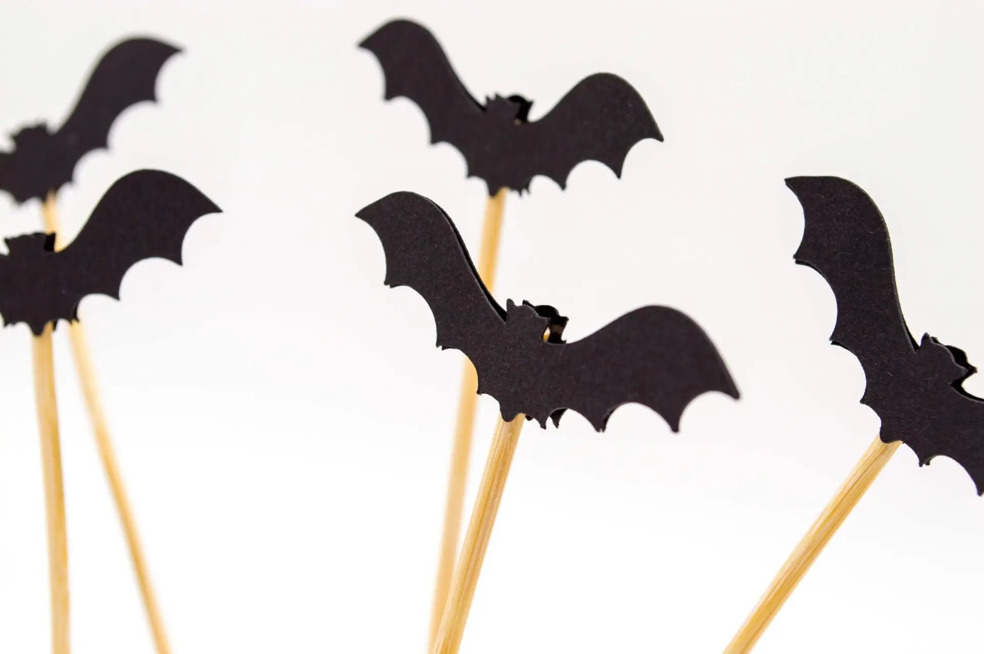 Silhouette cut-outs of bats on wooden sticks are arranged against a plain white background, crafting a minimalistic and spooky Halloween-themed decoration that's perfect for paper craft enthusiasts.