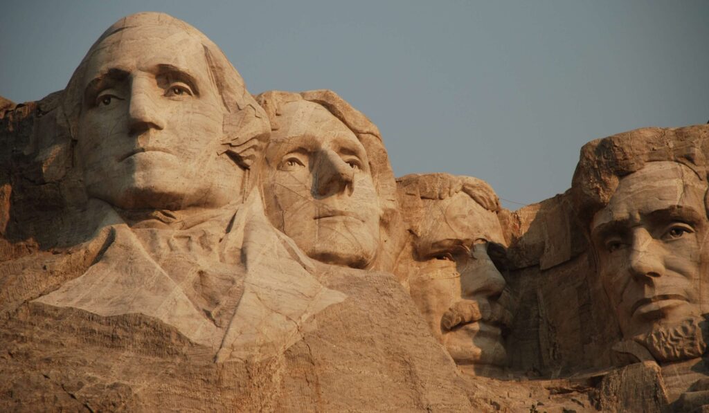 Mount Rushmore National Memorial showcases the sculpted faces of four U.S. presidents carved into a mountainside. Under a clear, blue sky, these detailed stone carvings include facial features and prominent historical figures, offering fascinating history trivia for kids to explore.