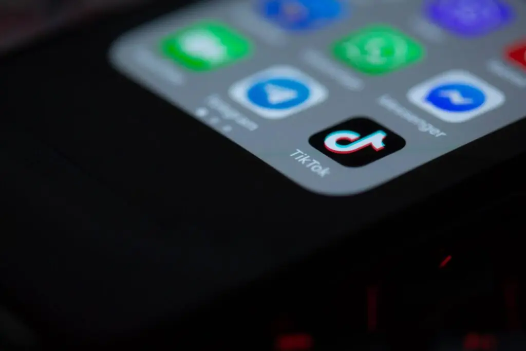 A close-up of a smartphone screen shows various app icons, including TikTok, Messenger, and WhatsApp. The screen is mostly dark with colorful icons at the top, subtly nodding to recent legislation impacting digital platforms like TikTok.