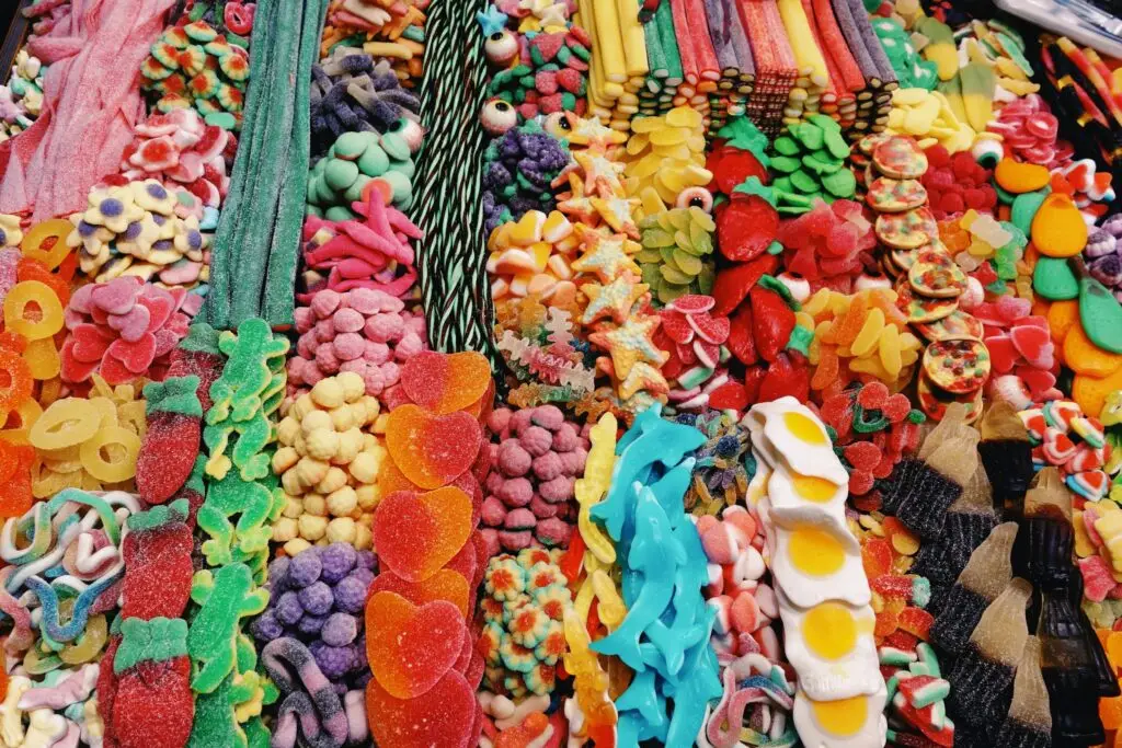 A colorful candy salad is displayed in neat rows, featuring an array of gummy sweets, licorice, sugar-coated treats, and multicolored candy strips. This vibrant and diverse confectionery spread delights the senses with its playful assortment.