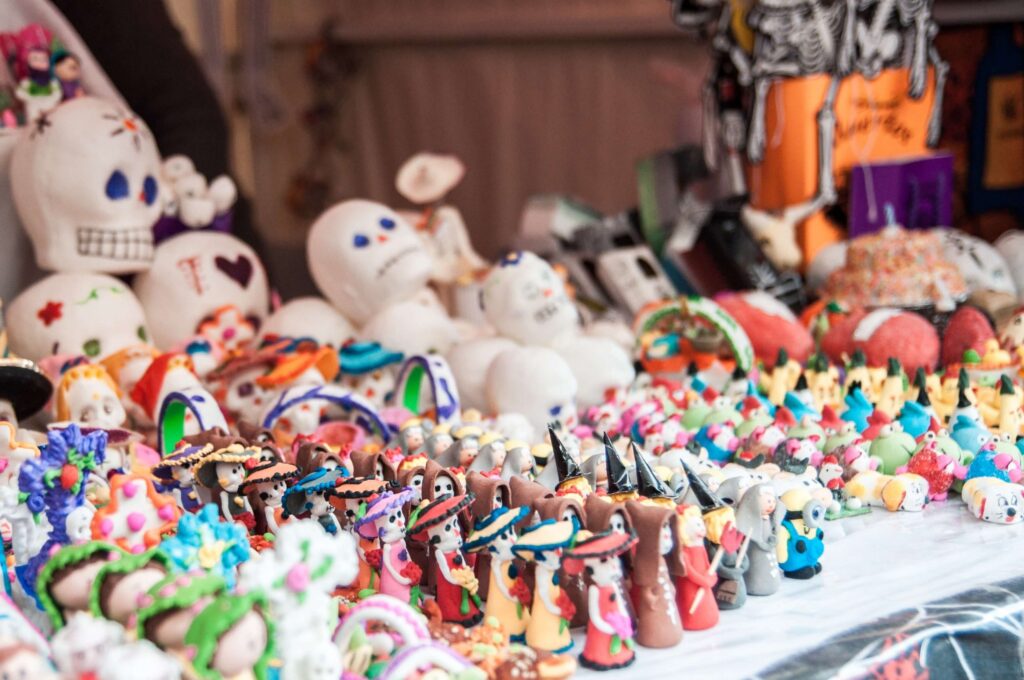 A vibrant display of colorful sugar skulls and figurines celebrates the Day of the Dead, showcasing a unique aspect of how Halloween is celebrated around the world. The assortment includes intricately adorned skulls and detailed figures in festive attire, all artfully arranged on a stall.