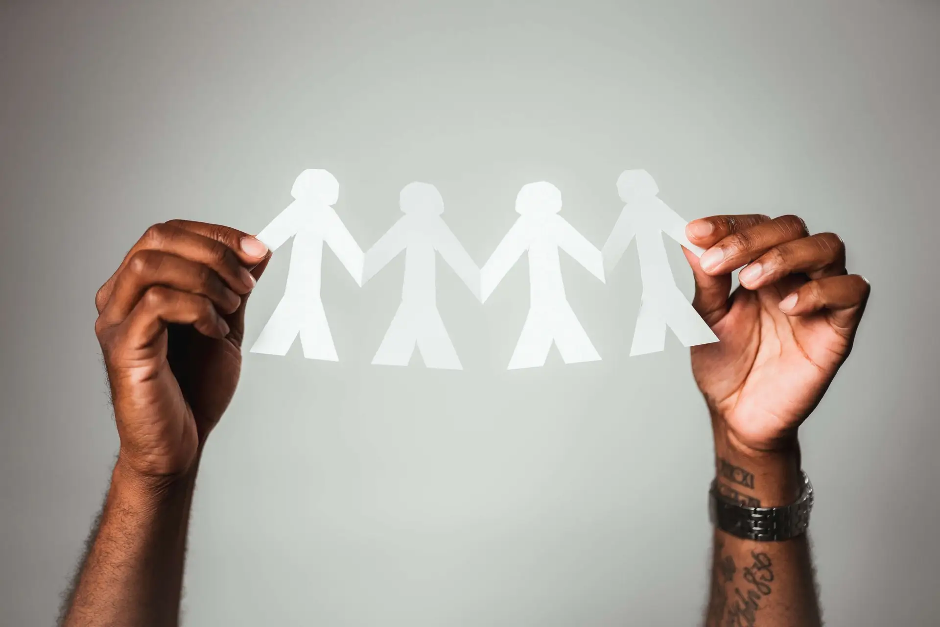 Hands holding a chain of four white paper cutout figures against a neutral background. The simple, stylized human shapes connect hand in hand, symbolizing unity and support—a fitting tribute to the spirit embodied by World Mental Health Day.