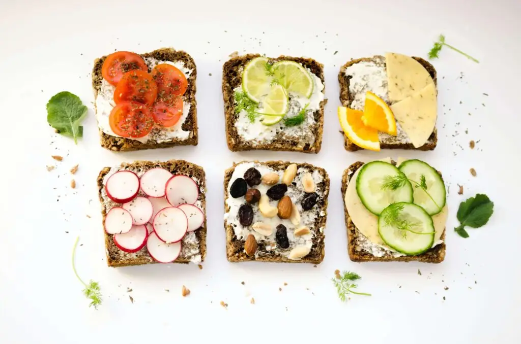 Six slices of bread with delightful toppings perfect as Thanksgiving snacks for kids: tomato, lime with black pepper, cheese and orange, cucumber, radish, and a mix of nuts and raisins. Garnished with parsley and crumbs on a white background.