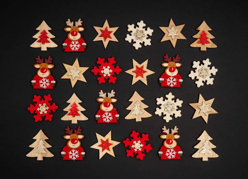 An arrangement of wooden Christmas decorations on a black background, resembling a festive Christmas breakfast charcuterie board. The display includes reindeer, red and white snowflakes, stars, and Christmas trees laid out in a grid pattern.