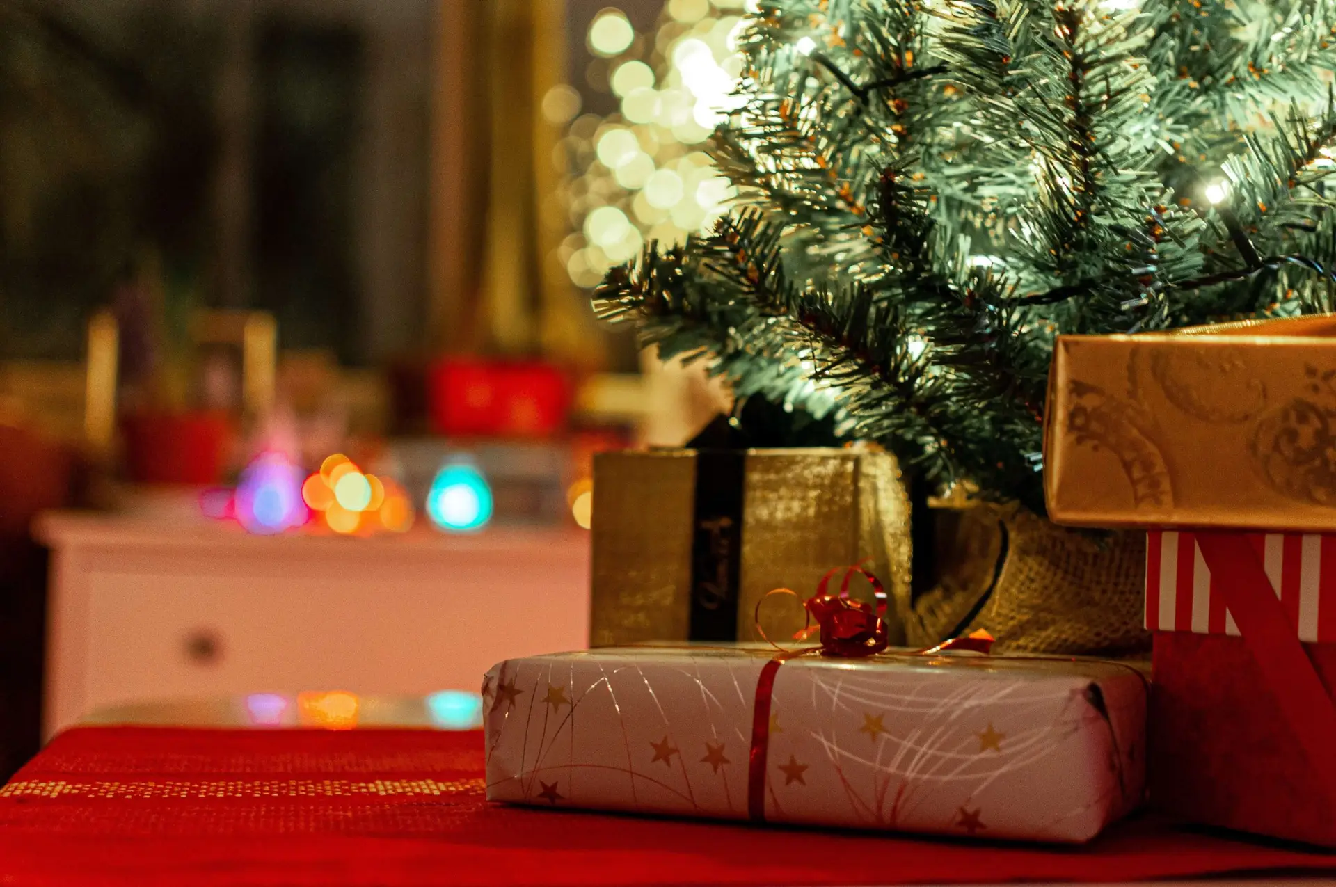 A festive scene with screen-free gifts wrapped under a decorated Christmas tree. Warm lights glow in the background, and a red tablecloth adds a holiday touch.