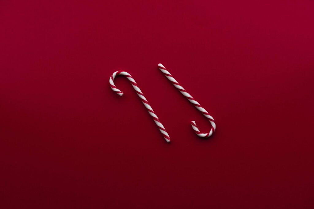 Two striped candy canes lying parallel on a deep red background, evoking the festive spirit of Christmas candy recipes.