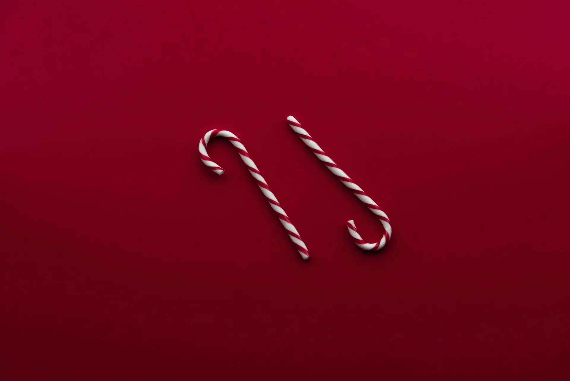 Two striped candy canes lying parallel on a deep red background, evoking the festive spirit of Christmas candy recipes.