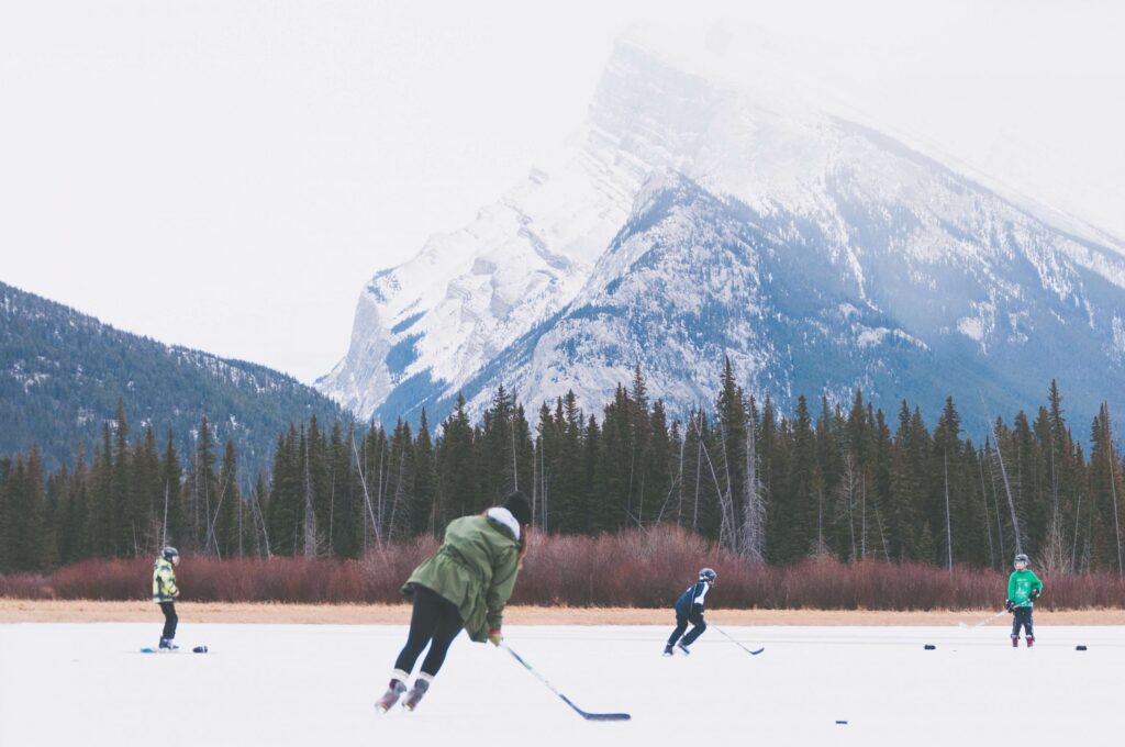 People playing ice hockey on a frozen lake with a backdrop of snow-covered mountains and dense pine forests share fun winter facts for kids. The scene has a wintry, overcast atmosphere.