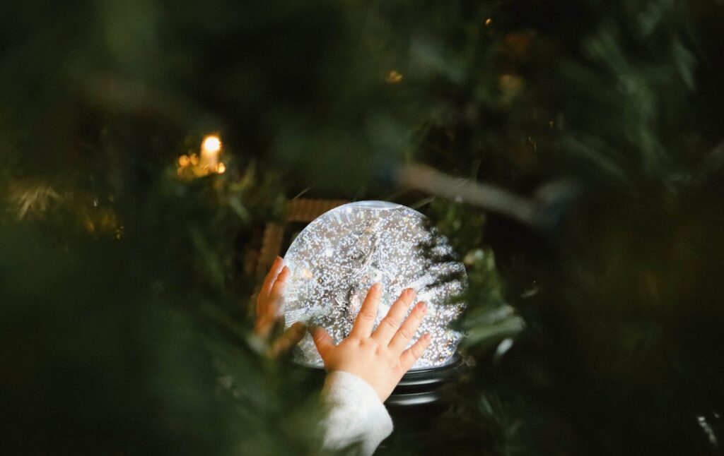 A child's hands touch a snow-dusted plate, surrounded by a soft focus of green foliage from a Christmas tree, creating a festive and cozy atmosphere perfect for inspiring winter art projects for kids.