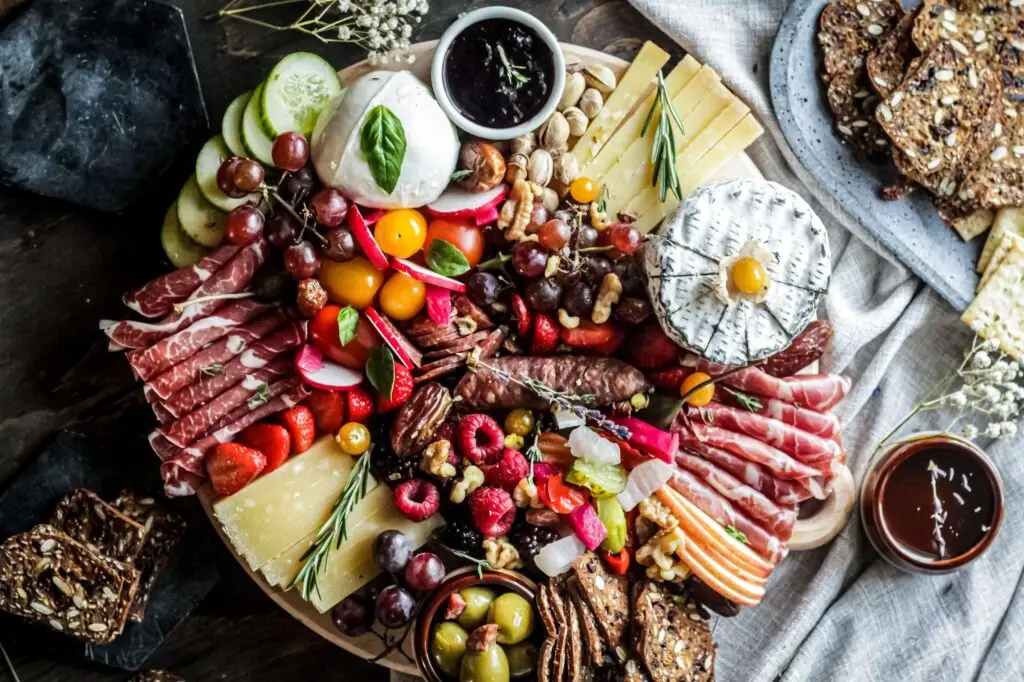 A vibrant Christmas wreath charcuterie board filled with assorted cheeses, cured meats, fresh fruits, nuts, olives, and crackers. The festive arrangement includes berries, grapes, and decorative sprigs of rosemary, crafting an appetizing and colorful spread.