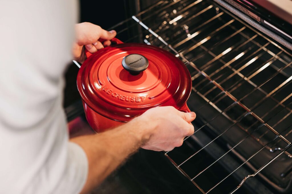 someone putting a red le creuset french oven into the oven