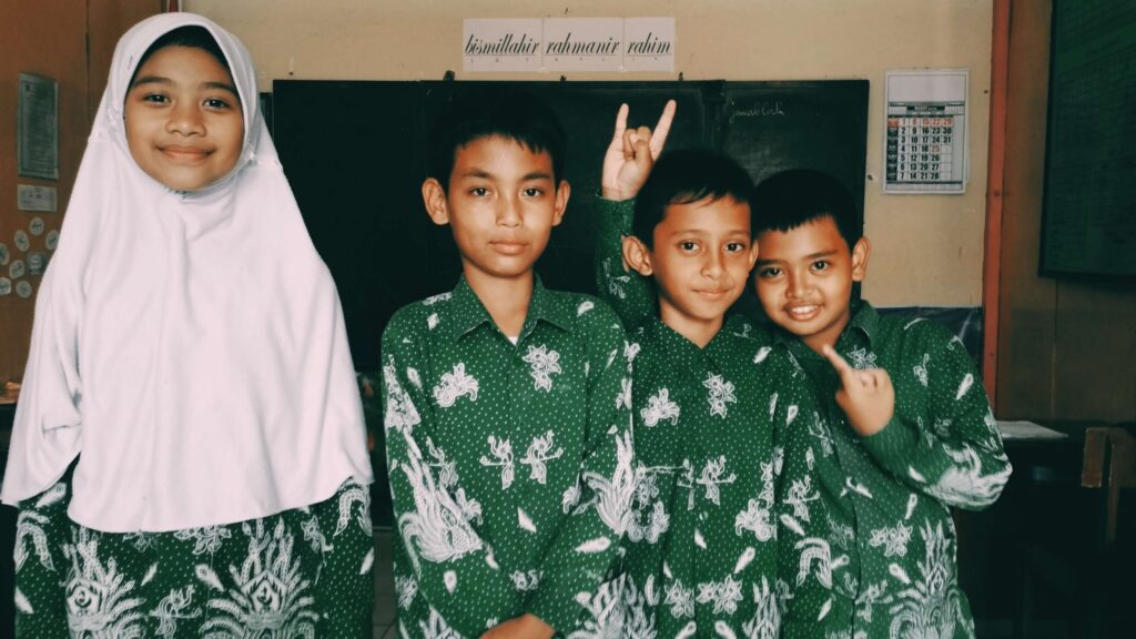 four kids in a classroom smiling for the camera