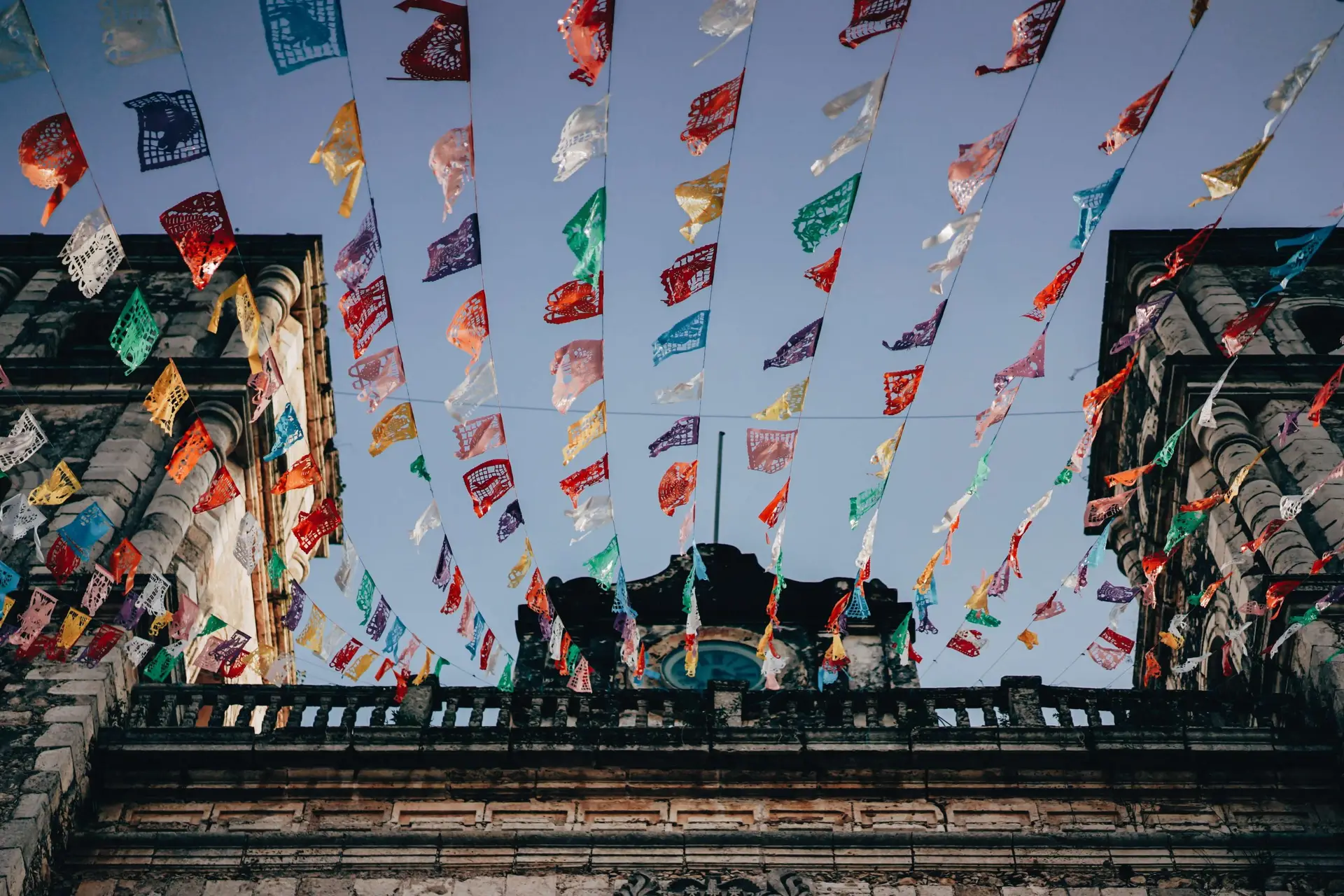 Colorful papel picado banners hang overhead between two stone buildings against a clear blue sky, echoing the festive atmosphere reminiscent of Mexico's vibrant Christmas celebrations, where fun facts abound about uniquely joyous traditions.