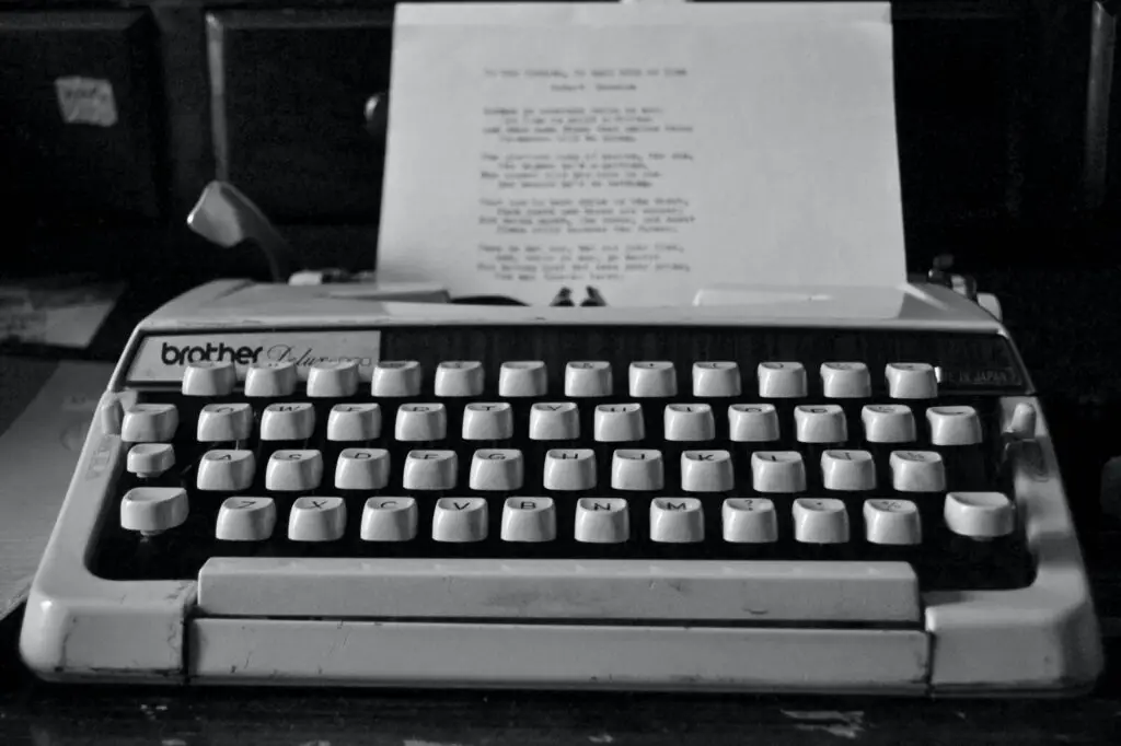 A black-and-white image of a vintage Brother typewriter holds a sheet of paper with whimsical Christmas poems for kids. The typewriter sits gracefully on a wooden desk, with drawers quietly lurking in the background.