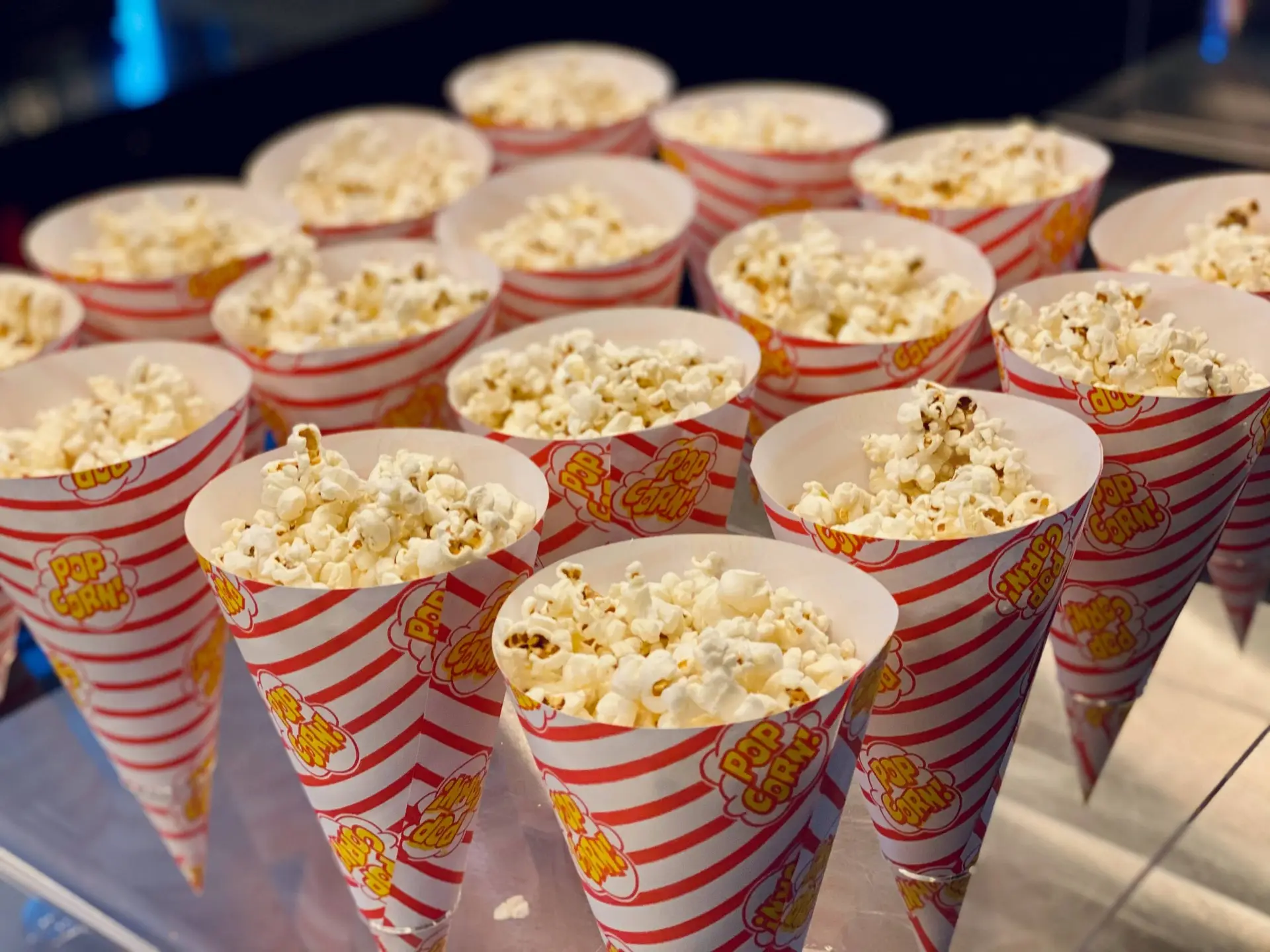 Rows of popcorn cones are neatly arranged, each filled with fluffy, white popcorn. Perfect for a Christmas movie night, the cones have a festive red and white striped pattern and are labeled with the words pop corn in a playful font.